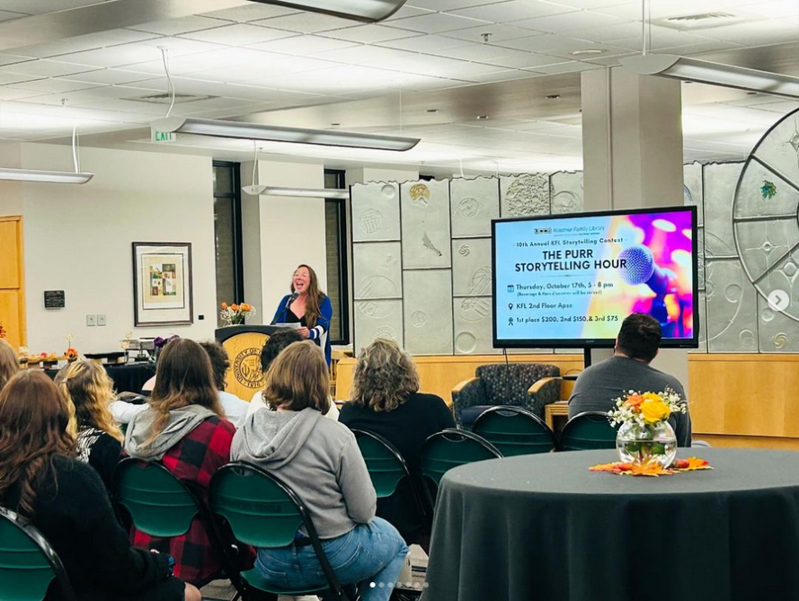 A contestant at the storytelling contest speaking at a podium in front of an audience in the 2nd floor library apse.