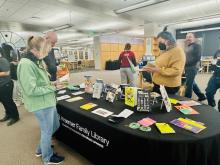 Patrons standing around a round table browsing the new zine collection.